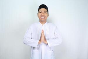 asian muslim man smiling to give greeting in eid mubarak celebration and welcoming ramadhan isolated on white background photo