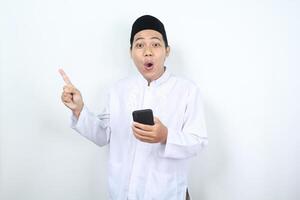 sorprendido musulmán asiático hombre señalando dedos aparte con participación móvil teléfono aislado foto