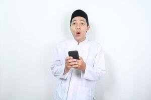 conmocionado asiático musulmán hombre mirando lejos con participación móvil teléfono aislado foto