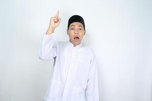 asian man muslim pointing above with shocked expression isolated on white background photo