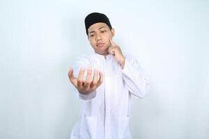 thoughtful asian muslim man show empty palm holding imaginary food plate with touching his chin isolated on white background photo