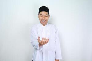 smiling asian muslim man showing empty palm at camera holding imaginary food plate isolated on white background photo