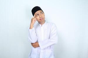 thoughtful asian muslim man looking above with hand touching his head isolated on white background photo