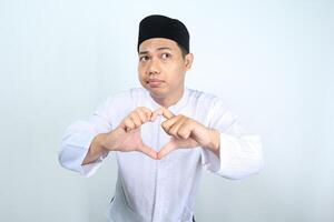 unhappy asian muslim man looking at camera and show heart shape isolated on white background photo