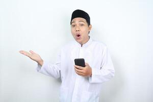 aturdido asiático musulmán hombre presentación aparte con participación móvil teléfono aislado foto