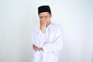 stressed asian man muslim rubbing his eyes with folded arm isolated on white background photo