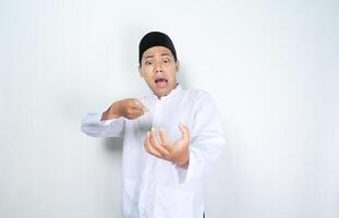 muslim asian man looks shocked while pointing to empty palm isolated on white background photo