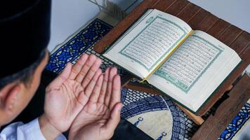 close up photo of a Muslim man reading the Quran on a prayer mat during the holy month of Ramadan.