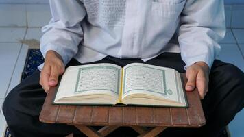 close up photo of a Muslim man reading the Quran on a prayer mat during the holy month of Ramadan.