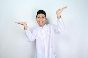 attractive muslim asian man presenting hand to above with smiling face isolated on white background, looking at camera photo