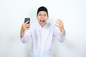 enojado musulmán asiático hombre participación teléfono con levantamiento mano y gritando a cámara foto