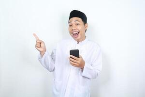 excited muslim asian man pointing hand to copy space with holding phone photo