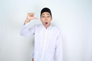 shocked asian man muslim pointing to him self with his thumbs isolated on white background photo