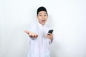 sorprendido musulmán asiático hombre participación móvil teléfono y levantamiento mano a presentación adelante a cámara aislado foto