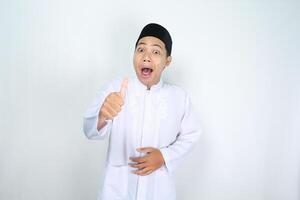 funny asian muslim man giving thumbs up with surprised expression isolated on white background photo