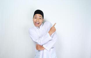 surprised asian muslim man pointing to copy space isolated on white background photo