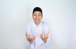 smiling asian muslim man showing empty palm at camera holding imaginary food plate isolated on white background photo