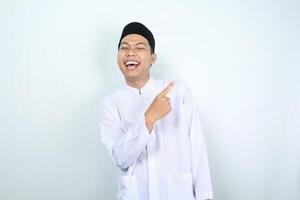 laughing asian muslim man pointing side isolated on white background photo