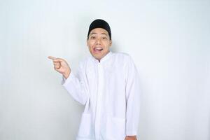 surprised asian muslim man pointing to copy space isolated on white background photo