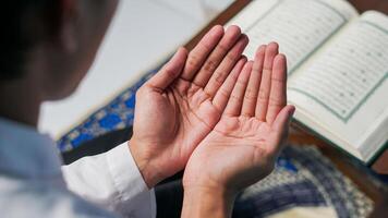 close up photo of a Muslim man praying and reading the Quran on a prayer mat