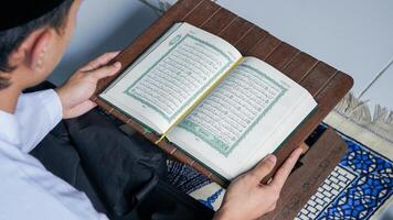 cerca arriba foto de un musulmán hombre leyendo el Corán en un oración estera durante el santo mes de Ramadán.