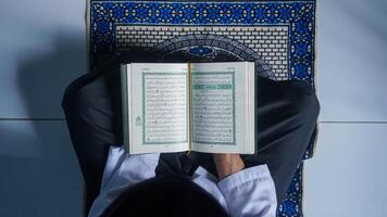 parte superior ver de un musulmán hombre leyendo el Corán en un oración estera mientras participación oración rosario. foto