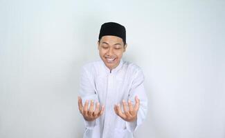 smiling asian muslim man showing empty palm at camera holding imaginary food plate isolated on white background photo