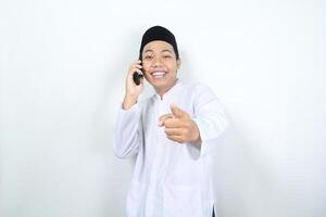 cheerful muslim asian man pointing forward to camera while speaking on his phone with smiling face isolated photo