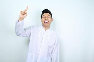 laughing asian muslim man pointing up isolated on white background photo