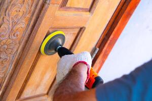 Close up hand middle-aged asian man uses a wood sander to polish a door at home. photo