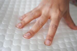 Hand touching and pressing orthopedic mattress on bed. photo