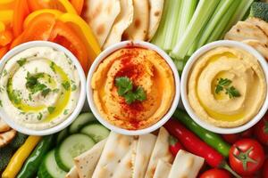 AI generated colourful hummus dips surrounded by various cut vegetables, pita bites, breadsticks photo