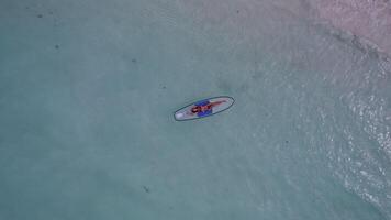 A girl is lying on a paddleboard in the ocean. The camera goes up. video