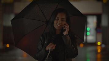 joven mujer hablando en móvil teléfono fuera de en el lluvia a noche video