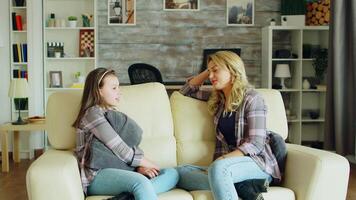 Beautiful young mother sitting on the couch in living room having a conversation with her daughter. video