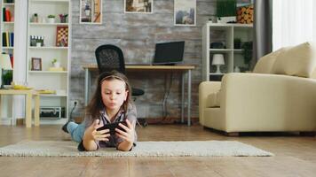 Little girl lying on the floor taking selfies with her smartphone. video