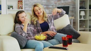 pequeño niña comiendo papas fritas mientras acecho película en televisión con su madre. madre y hija relajante. video