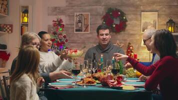 Little daughter at the table with the family celebrating christmas. Family eating tasty food. Traditional festive christmas dinner in multigenerational family. Enjoying xmas meal feast in decorated room. Big family reunion video