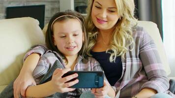 mooi jong moeder en haar dochter lachend terwijl aan het kijken een video Aan smartphone.