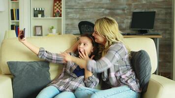 Cheerful mother and daughter taking a selfie with smartphone in living room. video