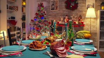 Kerstmis tafel decoratie met brandend kaarsen en traditioneel voedsel. Kerstmis viering in versierd kamer vol van wereldbol decoraties en Kerstmis boom met haard, groot feestelijk avondeten maaltijd voor groot familie video