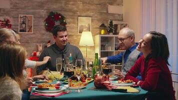 pequeno filhas sentado às a mesa com adultos a comemorar Natal. tradicional festivo Natal jantar dentro multigeracional família. desfrutando natal refeição festa dentro decorado sala. grande família reunião video