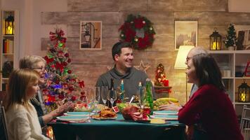 Woman arriving with chicken from the oven for christmas celebration with the family. Traditional festive christmas dinner in multigenerational family. Enjoying xmas meal feast in decorated room. Big family reunion video