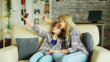 Little girl with braces sitting on the couch in living room taking a selfie with her mother. video