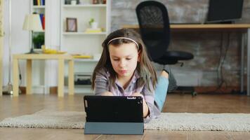 Cheerful little girl with braces lying on the floor carpet browsing on tablet computer. video