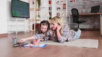 Little girl and mother bonding while she is drawing lying on the floor. video