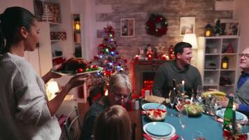 Follow shot of mother arriving with tasty chicking from oven to be eaten at christmas. Traditional festive christmas dinner in multigenerational family. Enjoying xmas meal feast in decorated room. Big family reunion video