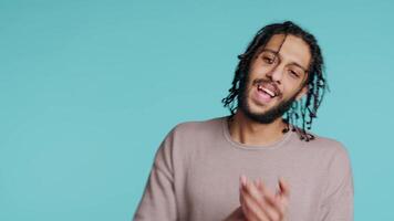 Approving smiling middle eastern man happily clapping hands, satisfied with accomplishments. BIPOC person cheering, doing praising gesture, isolated over blue studio background, camera B video