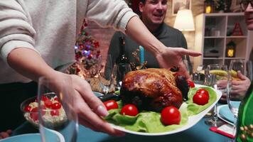 mujer con delicioso pollo para su grande familia celebrando Navidad. velas para invierno vacaciones. tradicional festivo Navidad cena en multigeneracional familia. disfrutando Navidad comida banquete en decorado habitación. grande familia reunión video