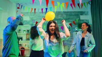 atraente jovem mulher festa com dela amigos enquanto segurando uma balão. selvagem Faculdade festa com uma quarto cheio do néon luzes, discoteca bola e álcool video